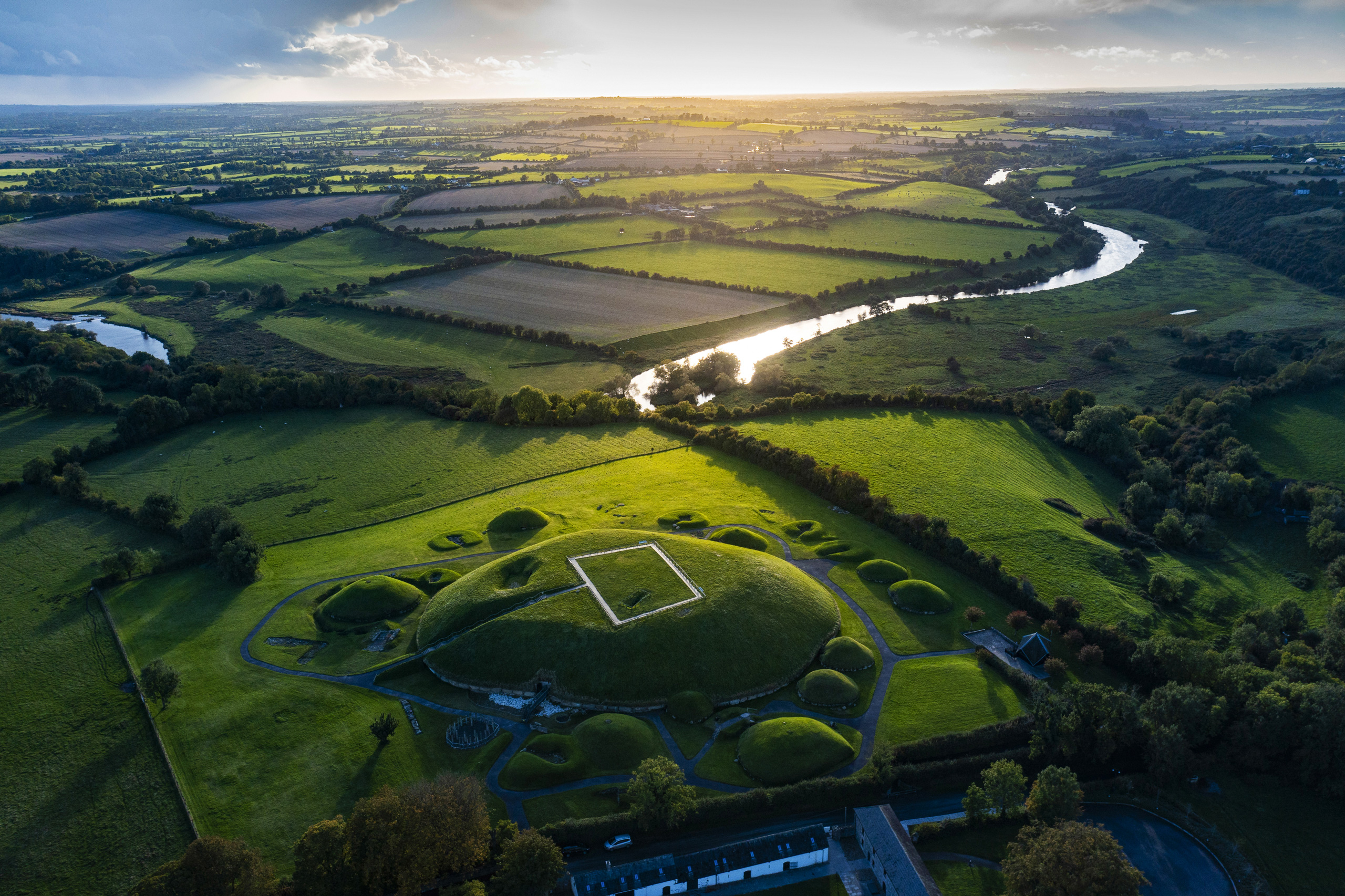 Aerial view of the Newgrange passage tomb in the Boyne Valley, surrounded by lush green fields, with a winding river visible in the distance.