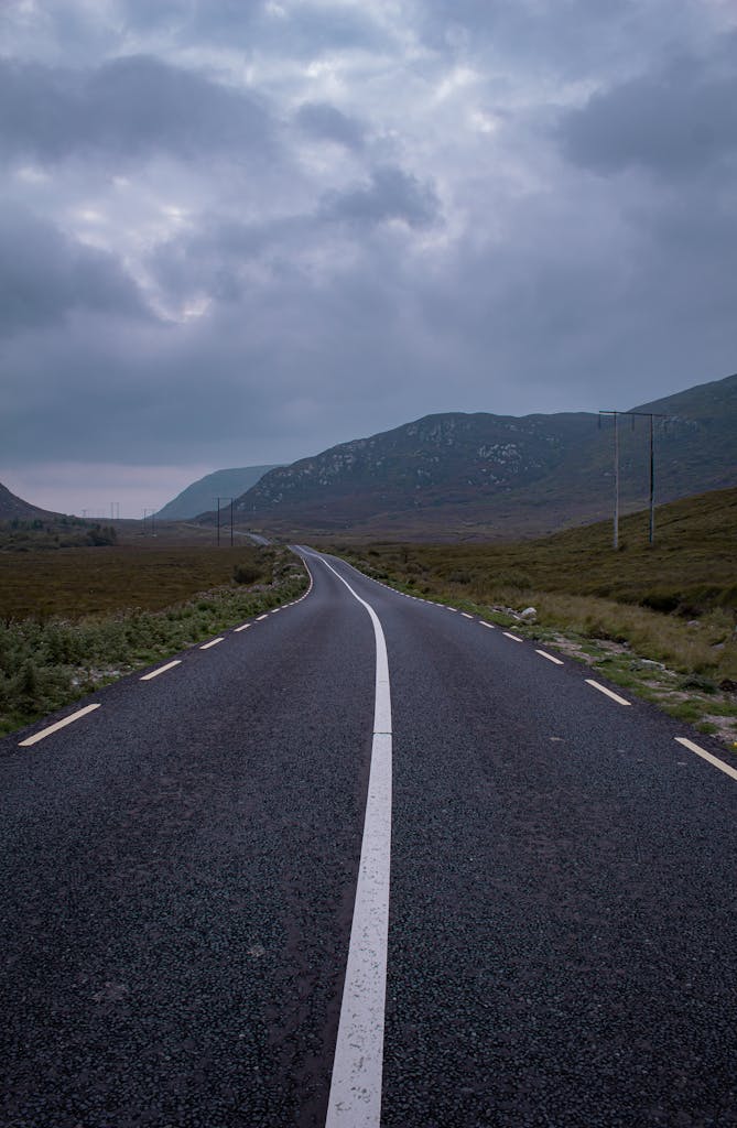Cobh, Co Cork A serene asphalt road in Roscommon, Ireland, cuts through lush countryside under a moody sky.