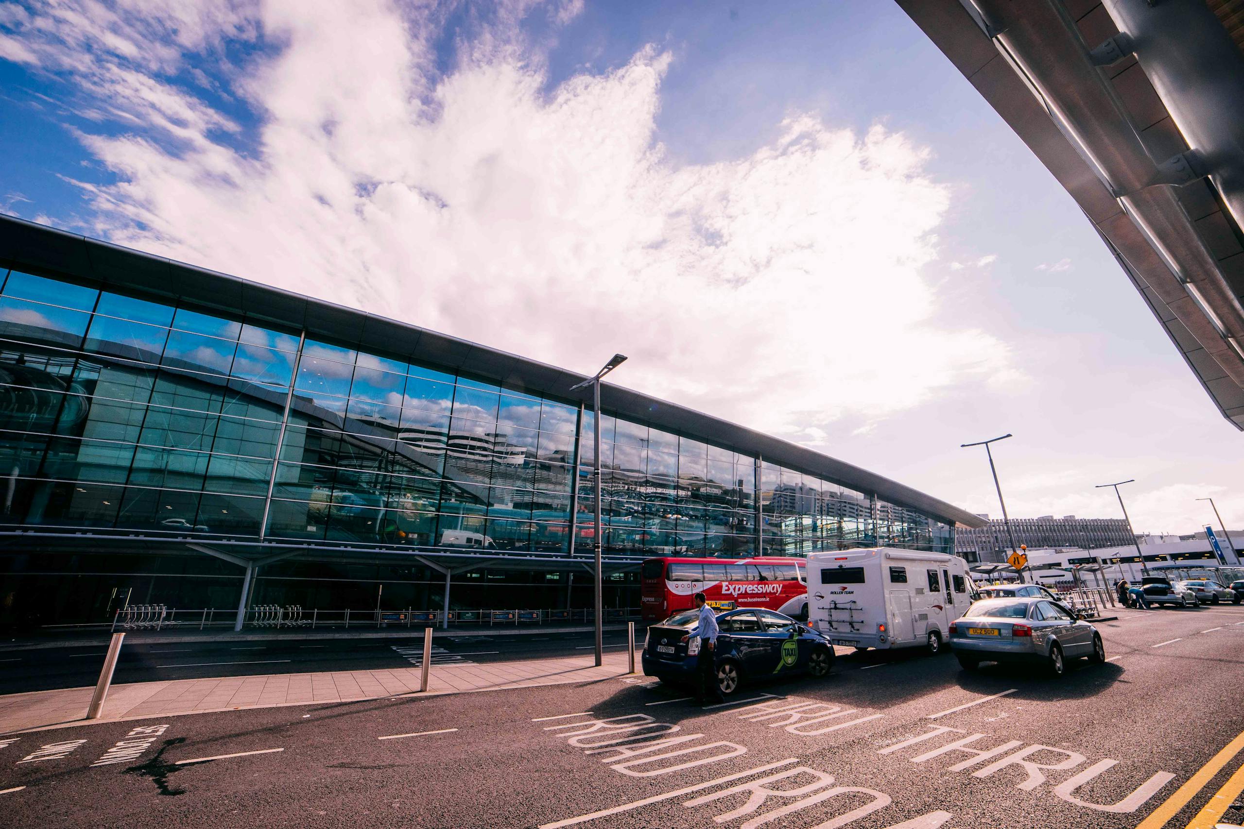 Daytime view of the modern terminal building at Dublin Airport, Ireland, with cars and buses parked outside.
